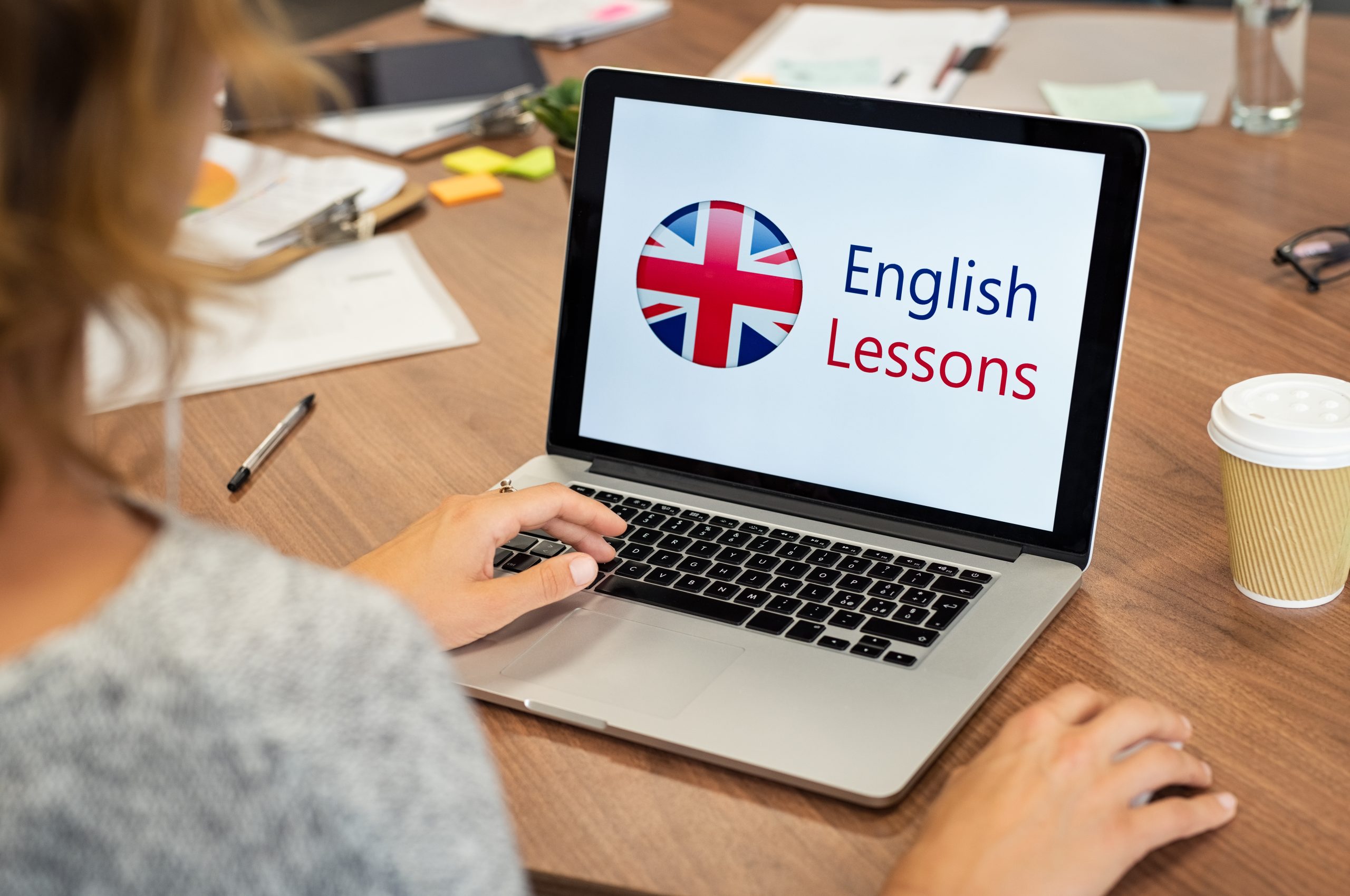 Mature woman learning English online with computer at office. Laptop screen of woman displaying english lessons poster with British flag. Closeup of student using laptop doing online course on english.